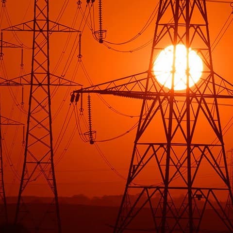 the sun sets behind power pylons