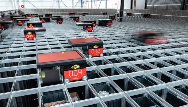 It works by using radio-controlled, battery-powered robots which move along a grid on top of stacks of bins. When a picking order comes in, robots lift bins from the stacks and deliver them to the picking station, where an operator verifies the contents and adds picks to the order.